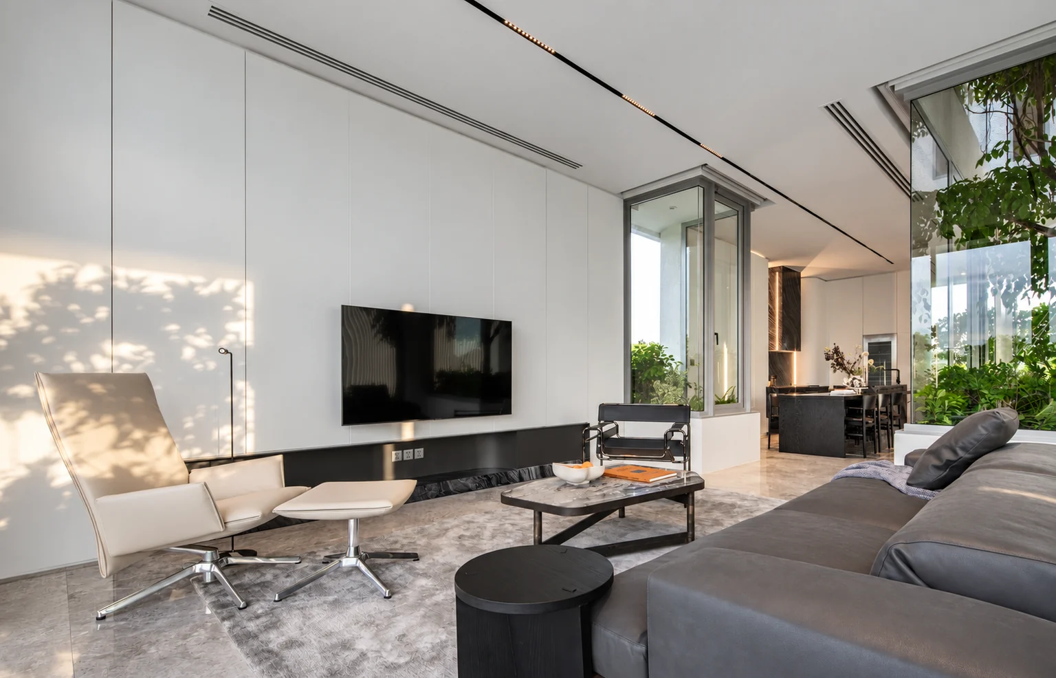 Sunlit residential living room with pale walls, grey seating and garden views.