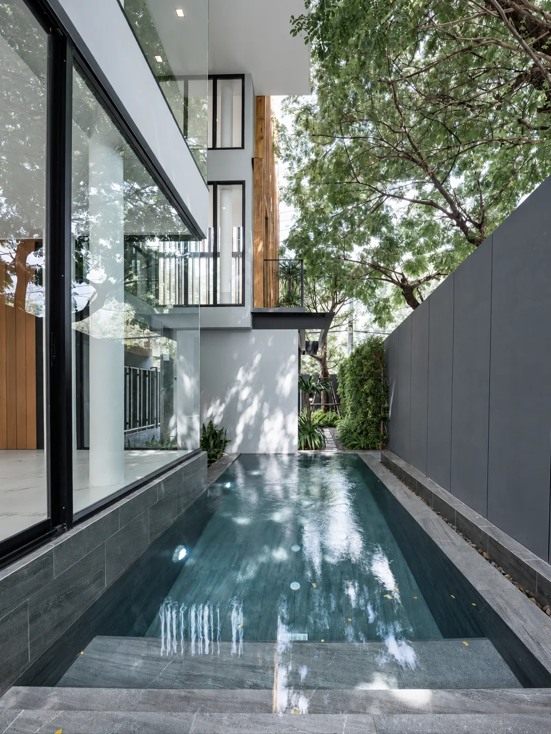 Glazing and a pool beside a tree-shaded courtyard in a project developed by Tom Jakkapat