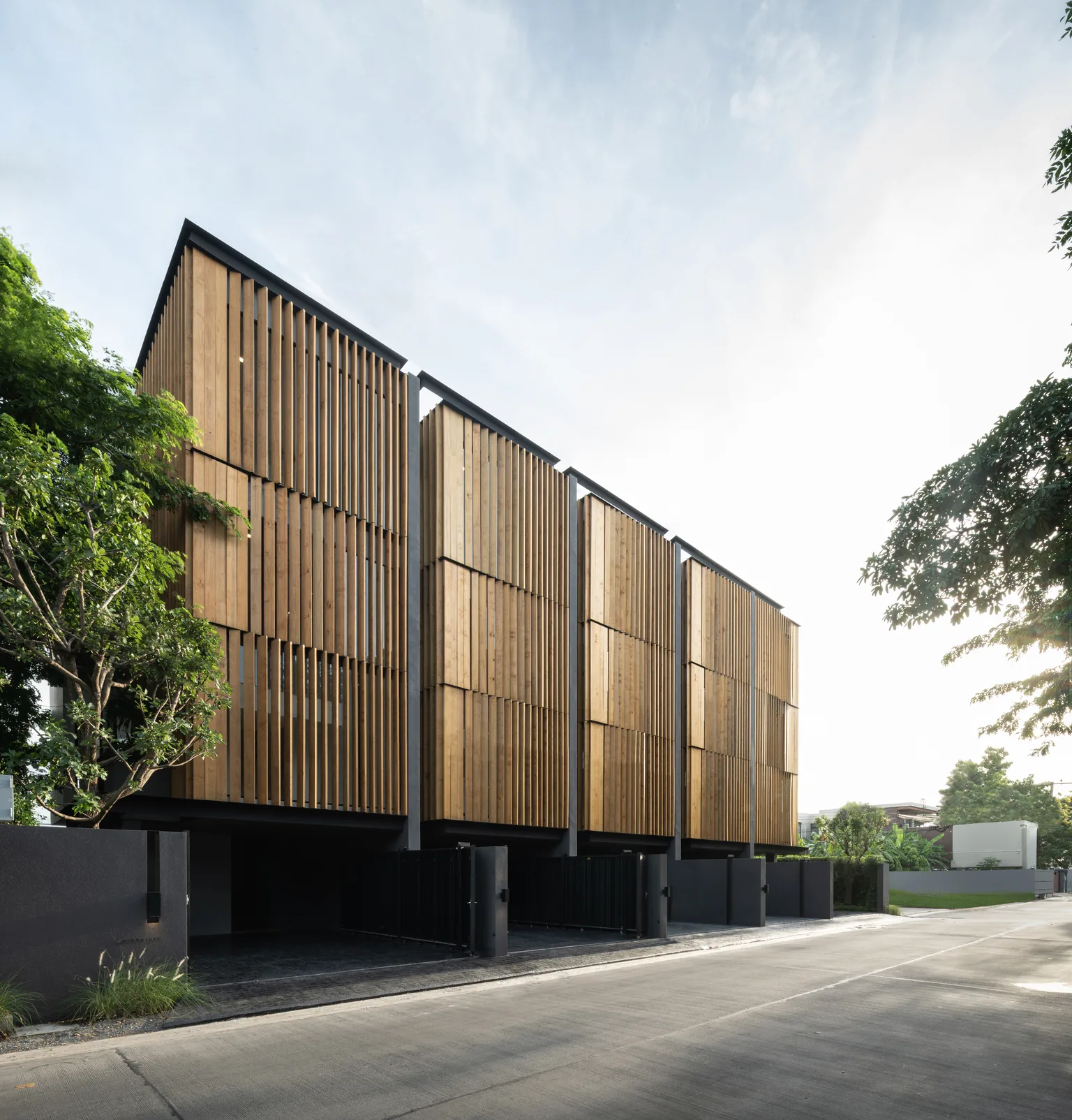 Street view of homes developed by Tom Jakkapat, with vertical timber screens and trees along the frontage.